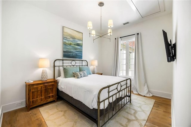 bedroom featuring visible vents, light wood-style flooring, an inviting chandelier, and baseboards