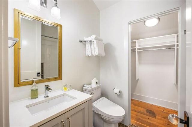 bathroom with toilet, vanity, baseboards, and wood finished floors