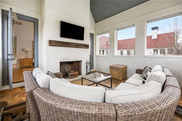 living area with lofted ceiling, an outdoor brick fireplace, and brick wall