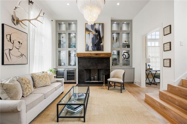 living room with wood finished floors, stairway, wine cooler, a fireplace, and a chandelier