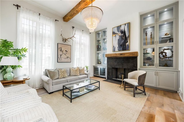 living area featuring beam ceiling, an inviting chandelier, light wood-style flooring, and a fireplace with flush hearth