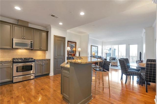 kitchen featuring a kitchen island, a kitchen bar, stainless steel appliances, light wood-type flooring, and light stone counters