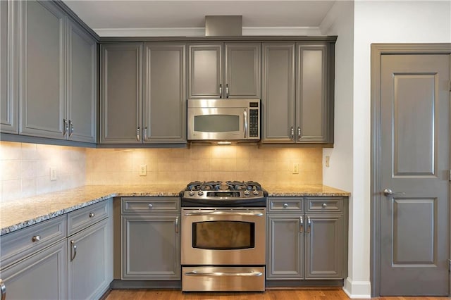 kitchen with light stone countertops, appliances with stainless steel finishes, tasteful backsplash, gray cabinets, and light hardwood / wood-style flooring