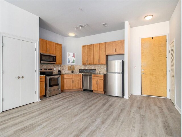 kitchen with appliances with stainless steel finishes, light hardwood / wood-style floors, and backsplash