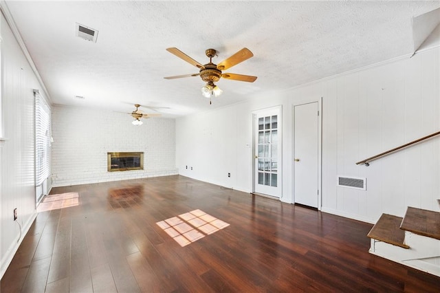 unfurnished living room featuring a textured ceiling, a brick fireplace, ceiling fan, dark wood-type flooring, and ornamental molding