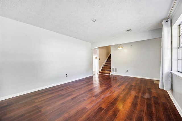 empty room with a textured ceiling, a healthy amount of sunlight, and dark hardwood / wood-style flooring