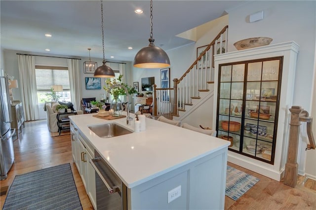 kitchen with stainless steel dishwasher, a sink, an island with sink, light wood finished floors, and recessed lighting