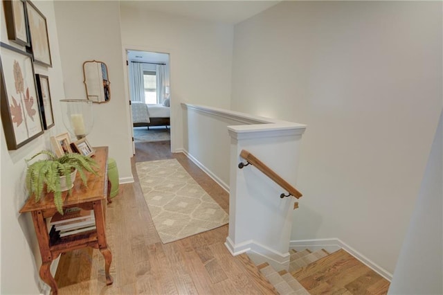 hallway with wood finished floors, an upstairs landing, and baseboards