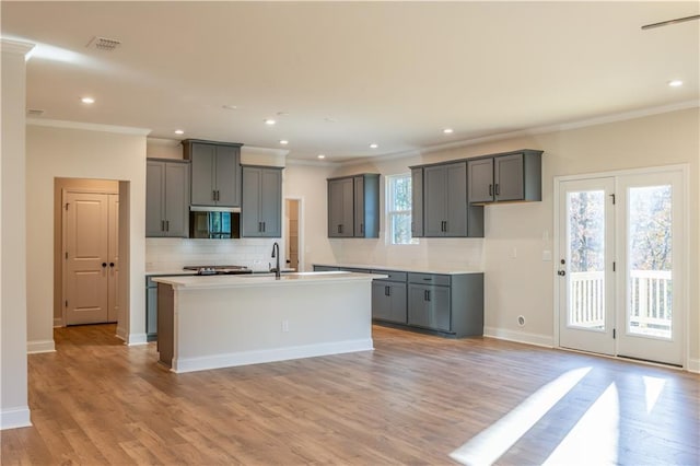 kitchen with tasteful backsplash, crown molding, gray cabinets, and an island with sink