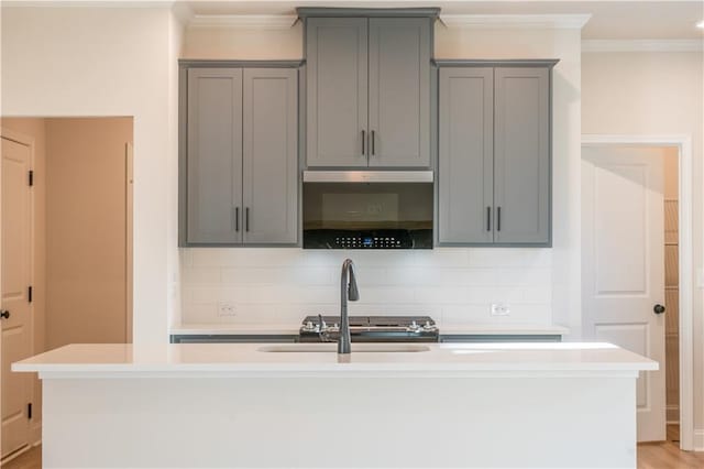 kitchen featuring an island with sink, sink, gray cabinetry, and ornamental molding