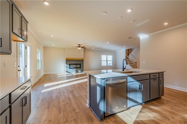 kitchen with sink, crown molding, light hardwood / wood-style flooring, stainless steel dishwasher, and an island with sink