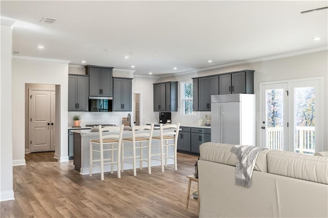 kitchen with gray cabinetry, high end refrigerator, backsplash, a kitchen breakfast bar, and a kitchen island with sink