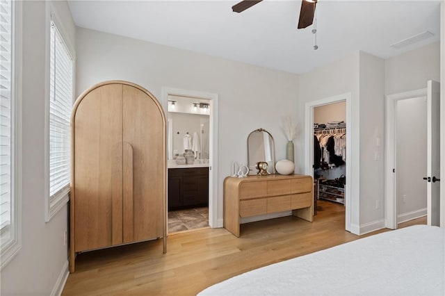 bedroom featuring light wood-style flooring, ensuite bath, a walk in closet, and multiple windows