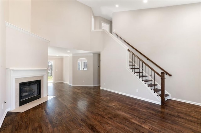 unfurnished living room featuring wood finished floors, a high ceiling, a premium fireplace, baseboards, and stairs