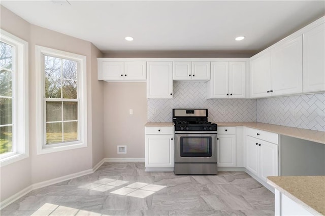 kitchen with baseboards, light countertops, stainless steel gas range, decorative backsplash, and white cabinetry