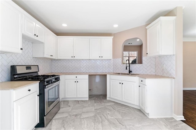 kitchen featuring a sink, stainless steel gas stove, white cabinetry, and light countertops