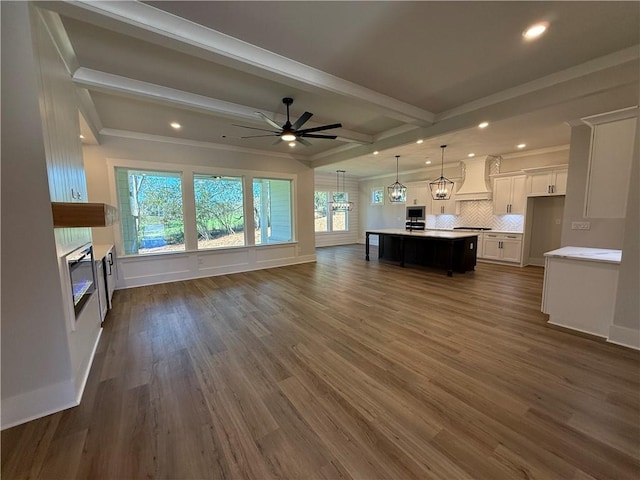 unfurnished living room featuring beam ceiling, ceiling fan with notable chandelier, and dark hardwood / wood-style floors