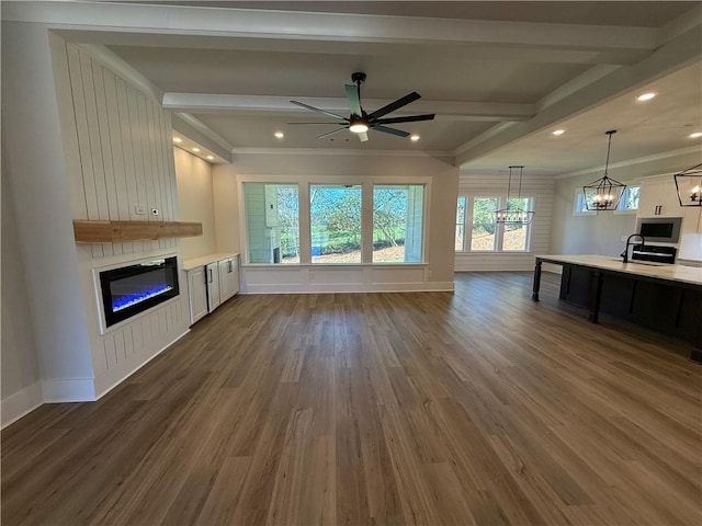 unfurnished living room featuring beam ceiling, dark hardwood / wood-style floors, crown molding, a fireplace, and ceiling fan with notable chandelier