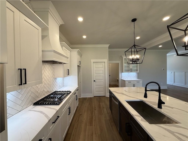 kitchen with light stone counters, decorative light fixtures, white cabinetry, and sink