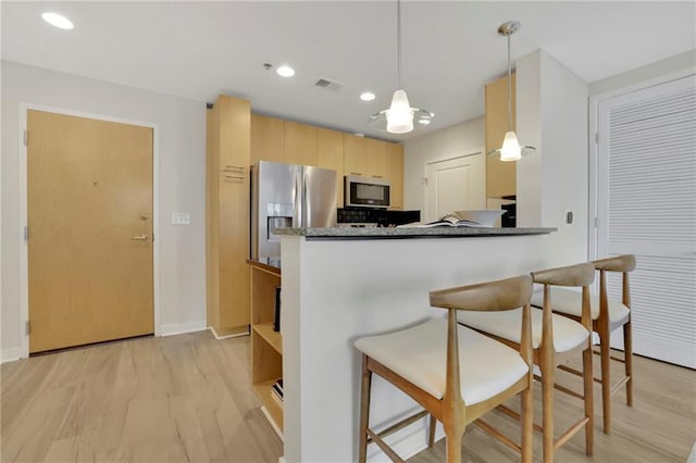 kitchen with light wood-type flooring, appliances with stainless steel finishes, light brown cabinets, pendant lighting, and kitchen peninsula