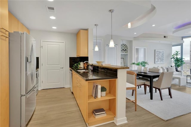 kitchen featuring appliances with stainless steel finishes, light brown cabinets, pendant lighting, light hardwood / wood-style floors, and kitchen peninsula