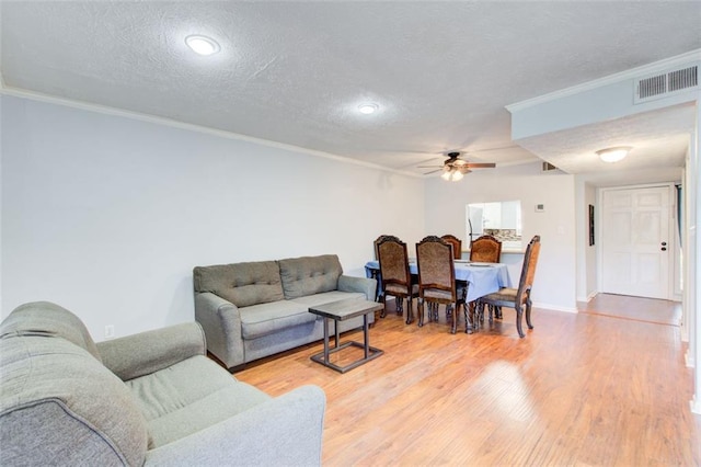 living room featuring ornamental molding, ceiling fan, a textured ceiling, and light wood-type flooring