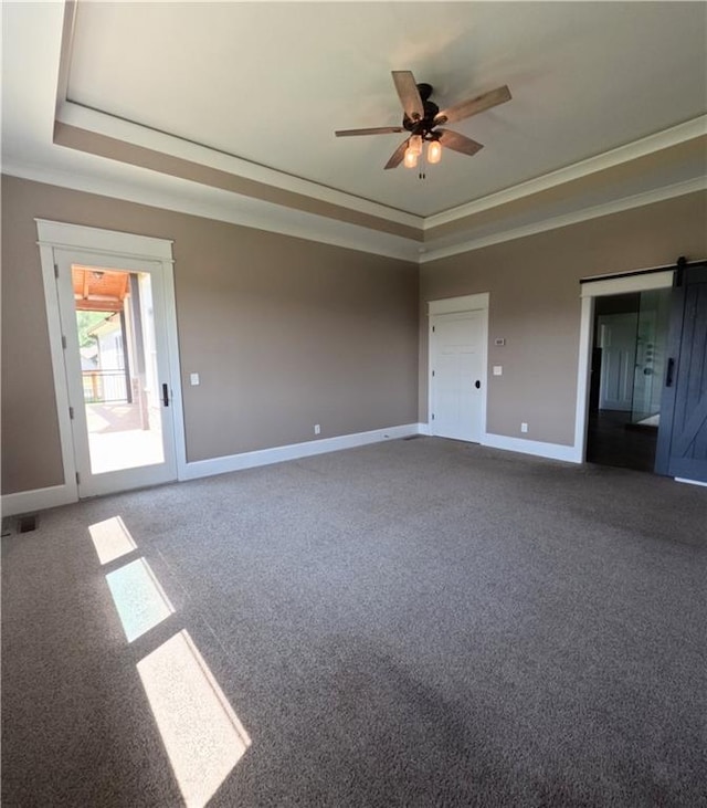 unfurnished bedroom with a barn door, a tray ceiling, carpet flooring, and ceiling fan