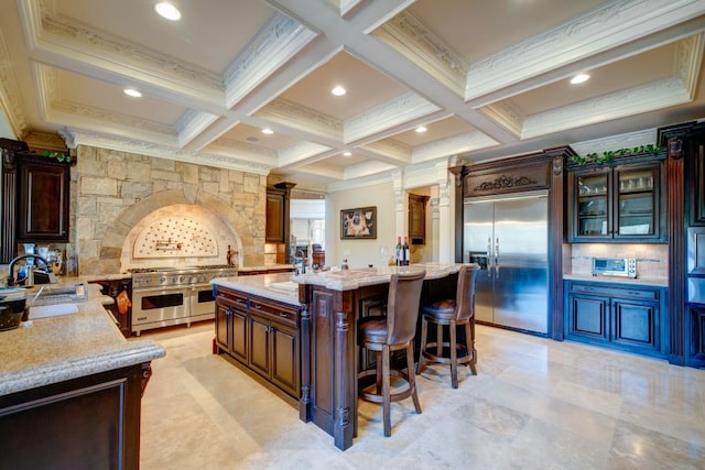 kitchen featuring high end appliances, a kitchen bar, sink, an island with sink, and light stone counters