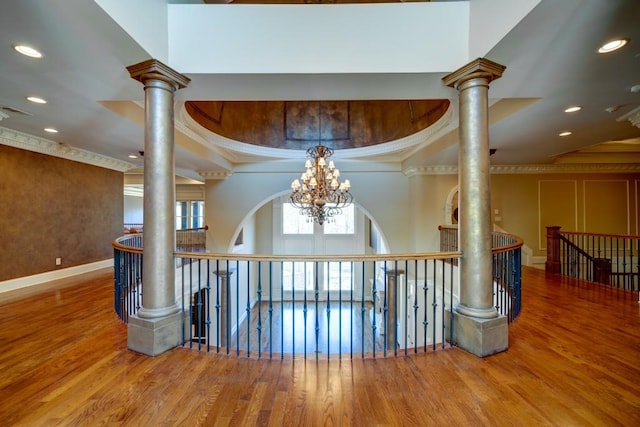 hallway with hardwood / wood-style flooring, an inviting chandelier, ornamental molding, and ornate columns