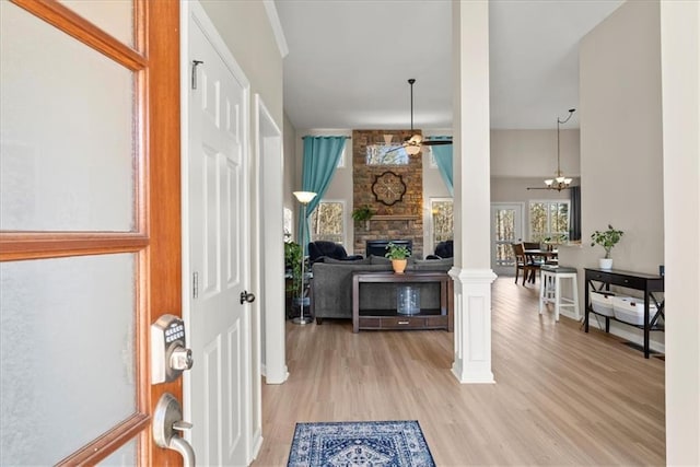 entrance foyer with light wood finished floors, ceiling fan, a fireplace, and ornate columns