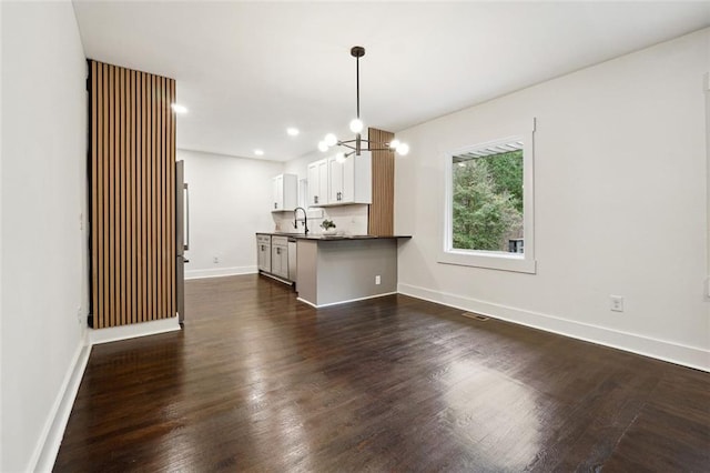 unfurnished living room with an inviting chandelier, dark wood-type flooring, and sink