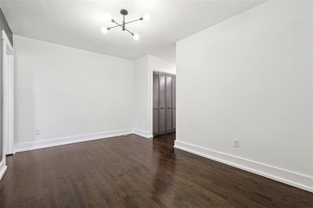 spare room featuring dark wood-type flooring and a notable chandelier