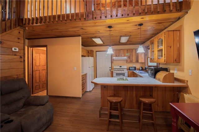 kitchen featuring kitchen peninsula, pendant lighting, white appliances, a breakfast bar area, and hardwood / wood-style flooring