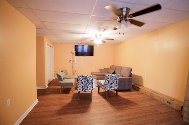 sitting room with ceiling fan, a drop ceiling, and wood-type flooring