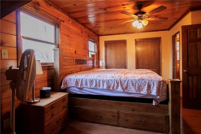 bedroom featuring ceiling fan, wooden ceiling, wood-type flooring, wooden walls, and two closets