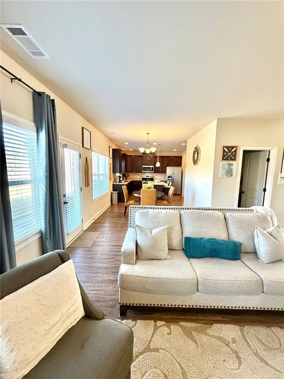 living area with visible vents, baseboards, dark wood-style floors, and a chandelier