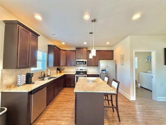 kitchen featuring visible vents, a kitchen bar, appliances with stainless steel finishes, independent washer and dryer, and a sink