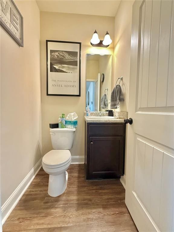 half bathroom featuring toilet, wood finished floors, and baseboards