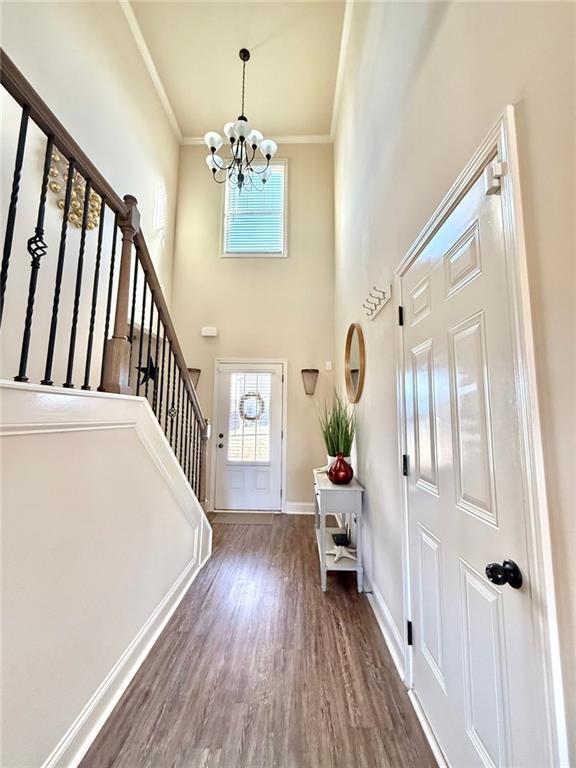 entrance foyer with stairway, wood finished floors, baseboards, crown molding, and a notable chandelier