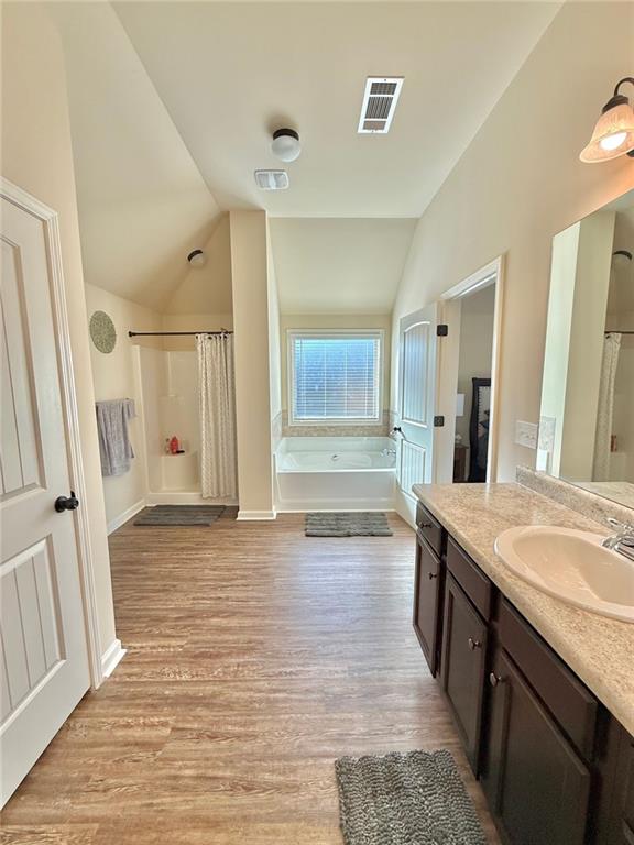 bathroom featuring visible vents, a garden tub, wood finished floors, and vaulted ceiling