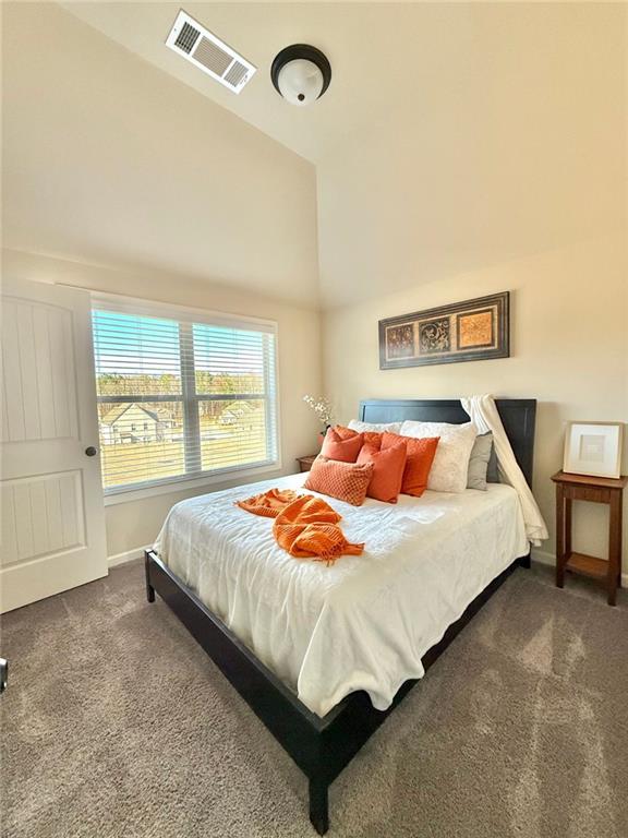 carpeted bedroom with visible vents, high vaulted ceiling, and baseboards