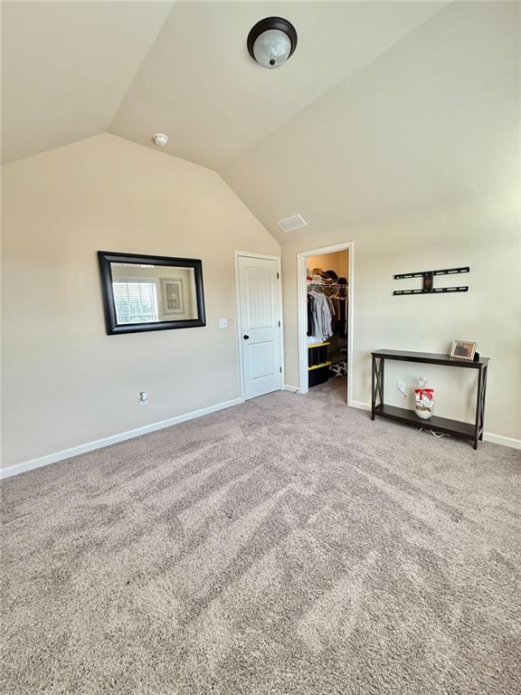 unfurnished bedroom with baseboards, carpet floors, lofted ceiling, a spacious closet, and a closet