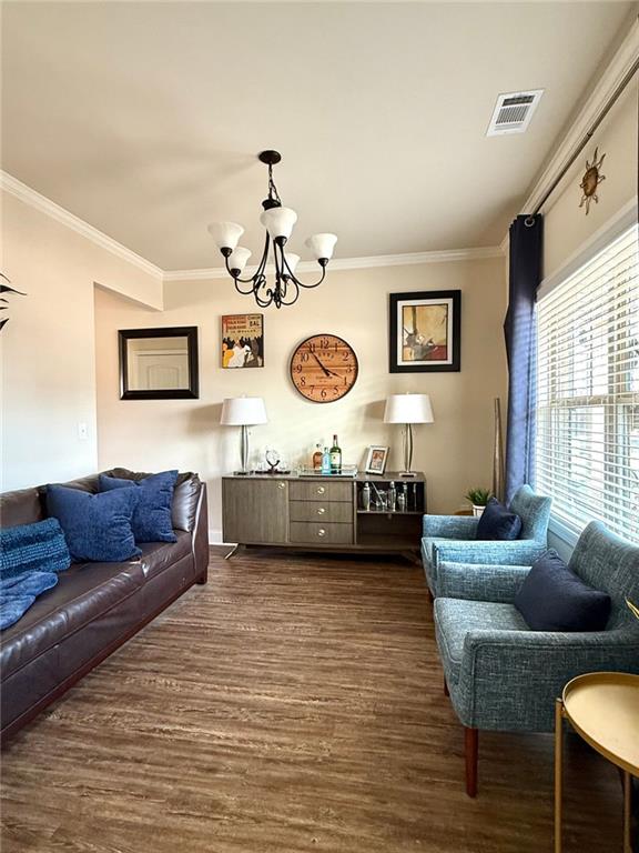 living room with a chandelier, visible vents, dark wood-style floors, and crown molding