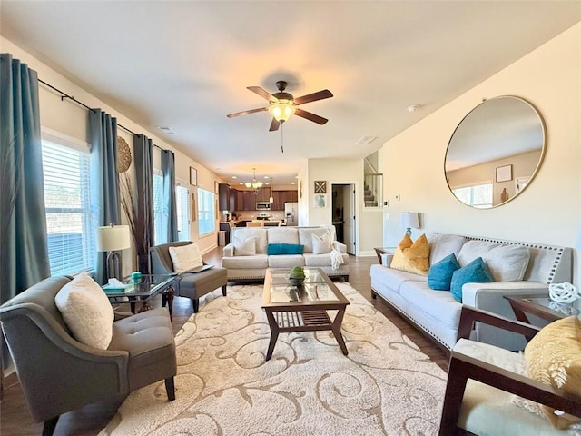 living area featuring baseboards, light wood-style flooring, and ceiling fan with notable chandelier