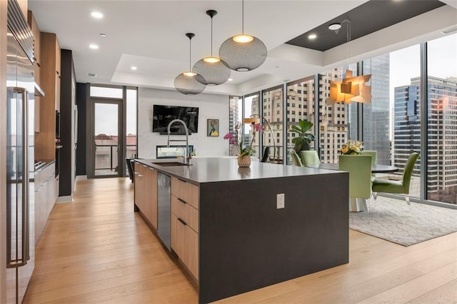 kitchen featuring dishwasher, an island with sink, dark countertops, decorative light fixtures, and a tray ceiling