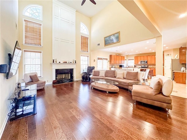 living room with a fireplace, light hardwood / wood-style flooring, ceiling fan, and a high ceiling