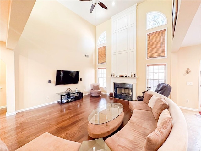 living room featuring a high ceiling, ceiling fan, a large fireplace, and light hardwood / wood-style floors