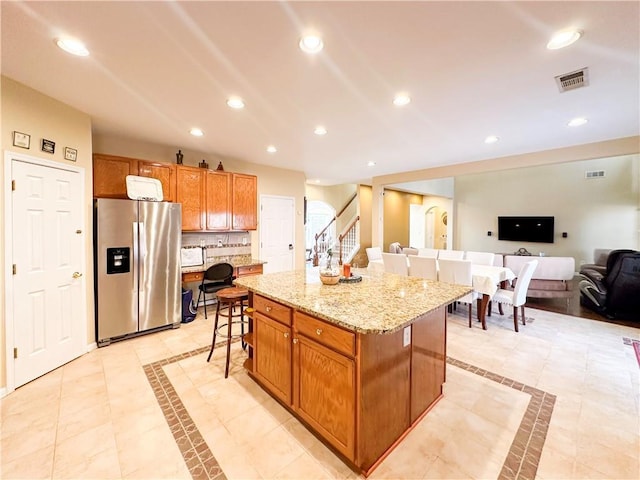 kitchen with stainless steel refrigerator with ice dispenser, a kitchen bar, light stone counters, a kitchen island, and backsplash