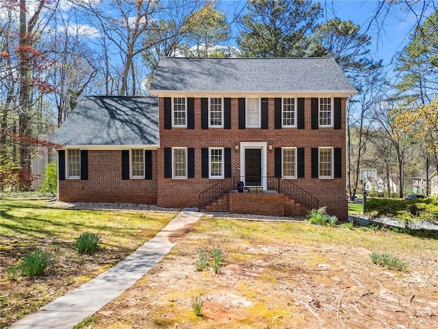 colonial inspired home with brick siding and a shingled roof