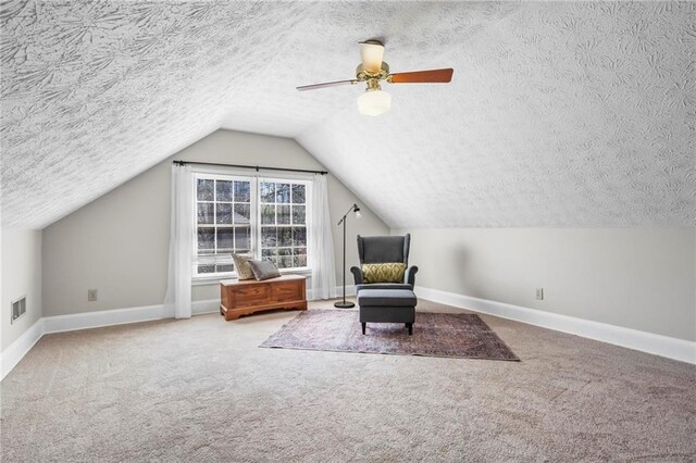 living area featuring a textured ceiling, visible vents, vaulted ceiling, baseboards, and carpet